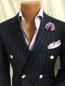 A man wearing a suit and tie with a purple flower pin.