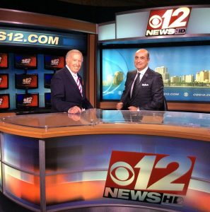 Two men in suits and ties are sitting at a news desk.