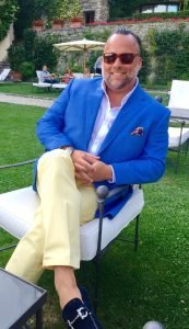 A man in blue jacket sitting on chair outside.