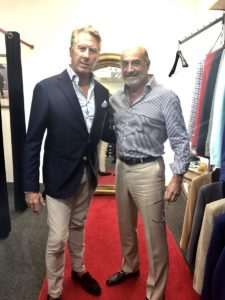 Two men posing for a picture in front of some clothes.