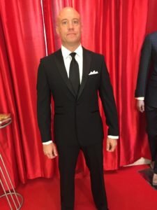 A man in a suit and tie standing on the red carpet.