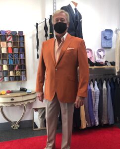 A man in an orange suit standing next to a wall of suits.
