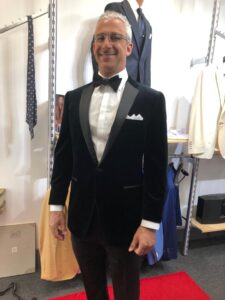 A man in a tuxedo standing next to some clothes.